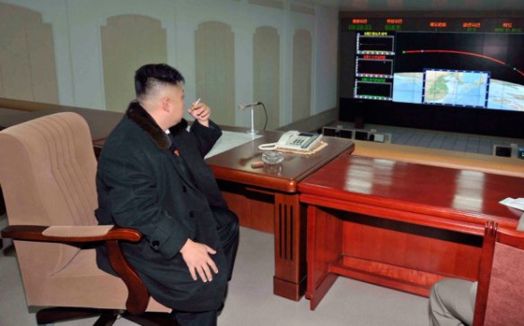 Image Source: AP. The Leader sits at more plain desks that look like a cheap set looking at what looks like a screen from an 80s sci fi film.